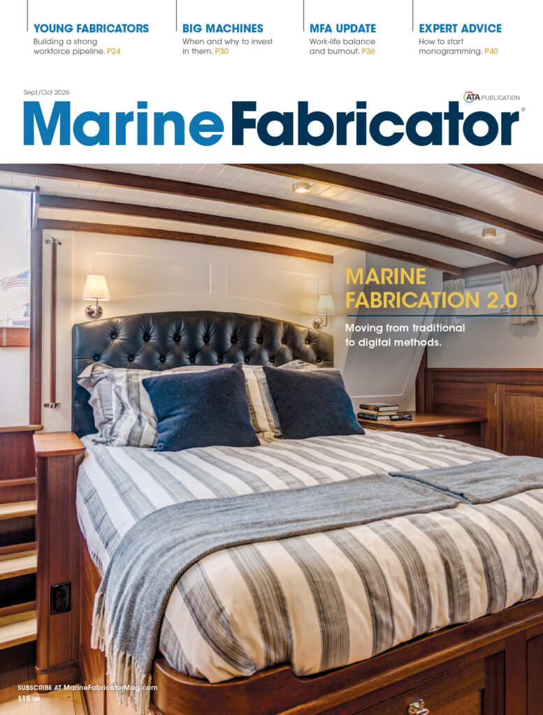 A cozy bedroom with a striped bedspread, wooden paneling, and soft lighting; featured in "Marine Fabricator" magazine's Sept/Oct 2016 issue.