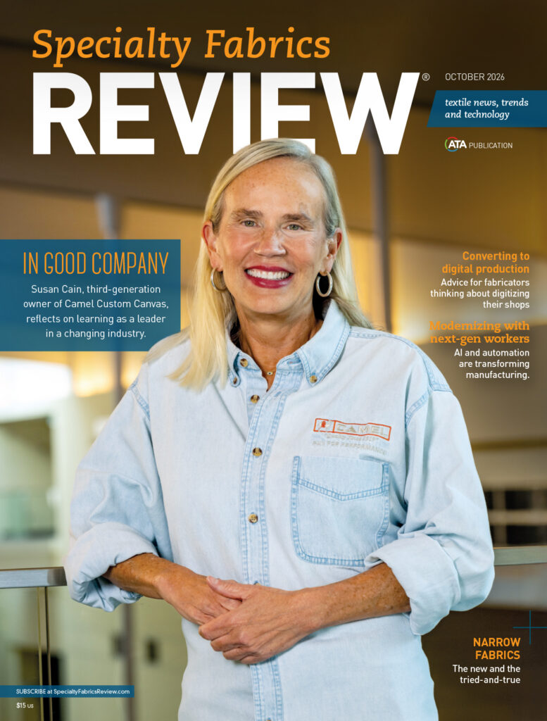 A smiling woman in a denim shirt stands in a modern interior, with a focus on textiles and manufacturing news in the background.
